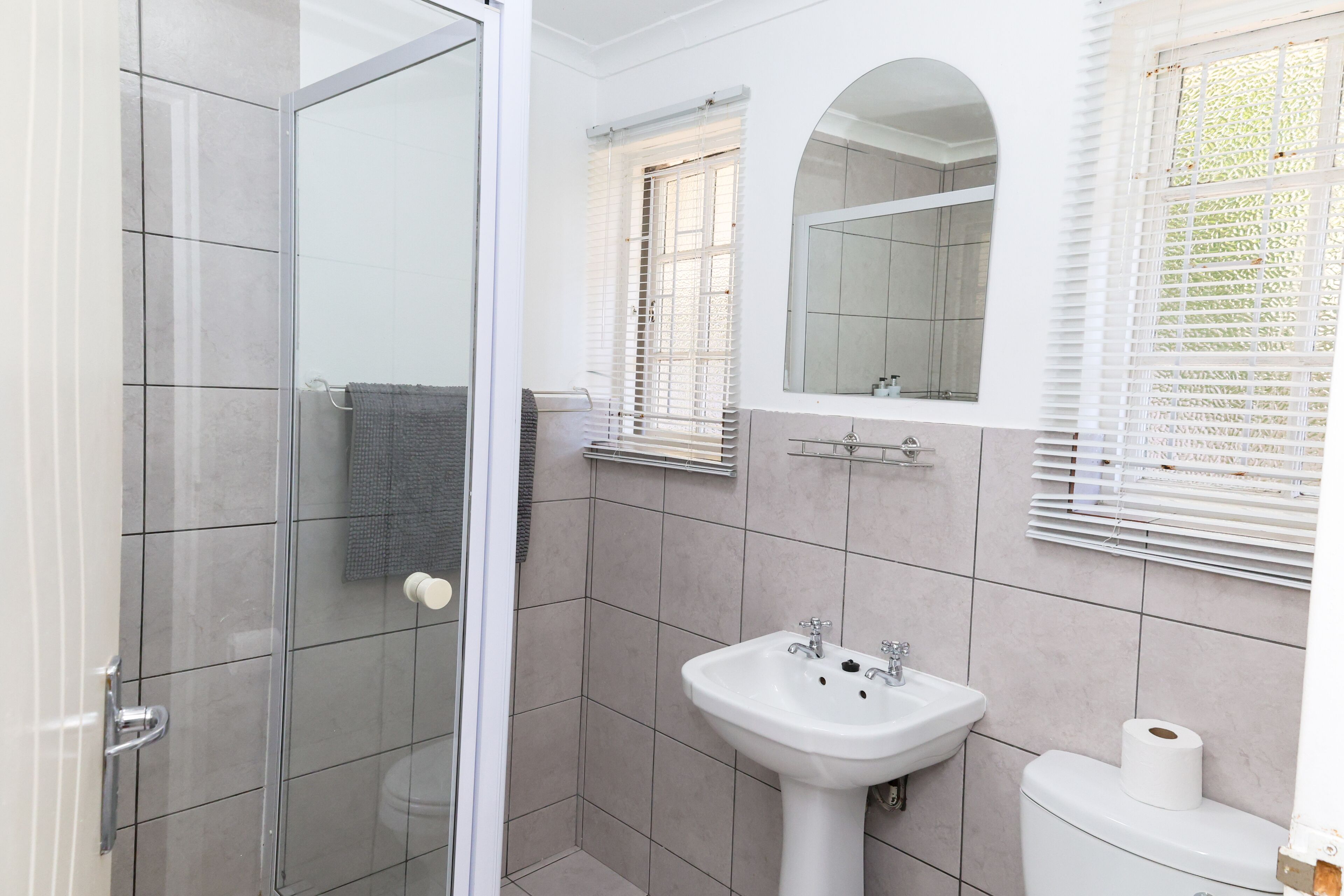 Une salle de bain avec une douche à parois de verre, un lavabo, des toilettes et une fenêtre avec des stores.