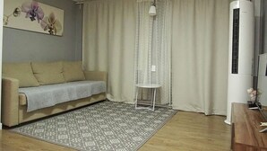 Olohuone, jossa on sohva, kuviollinen matto, pieni pöytä, seinälle asennettu ilmastointilaite ja ikkuna, jossa on verhot.