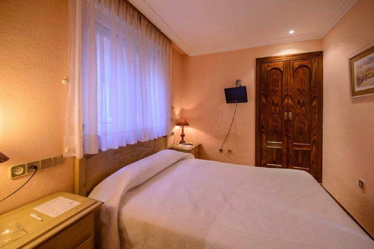 A hotel room with a bed, a nightstand, a lamp, a television, and a wooden door.