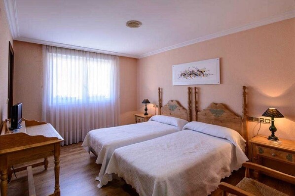 A hotel room with two beds, a desk, a television, and a window with curtains. - Hotel Rio Cea (Valderrueda)