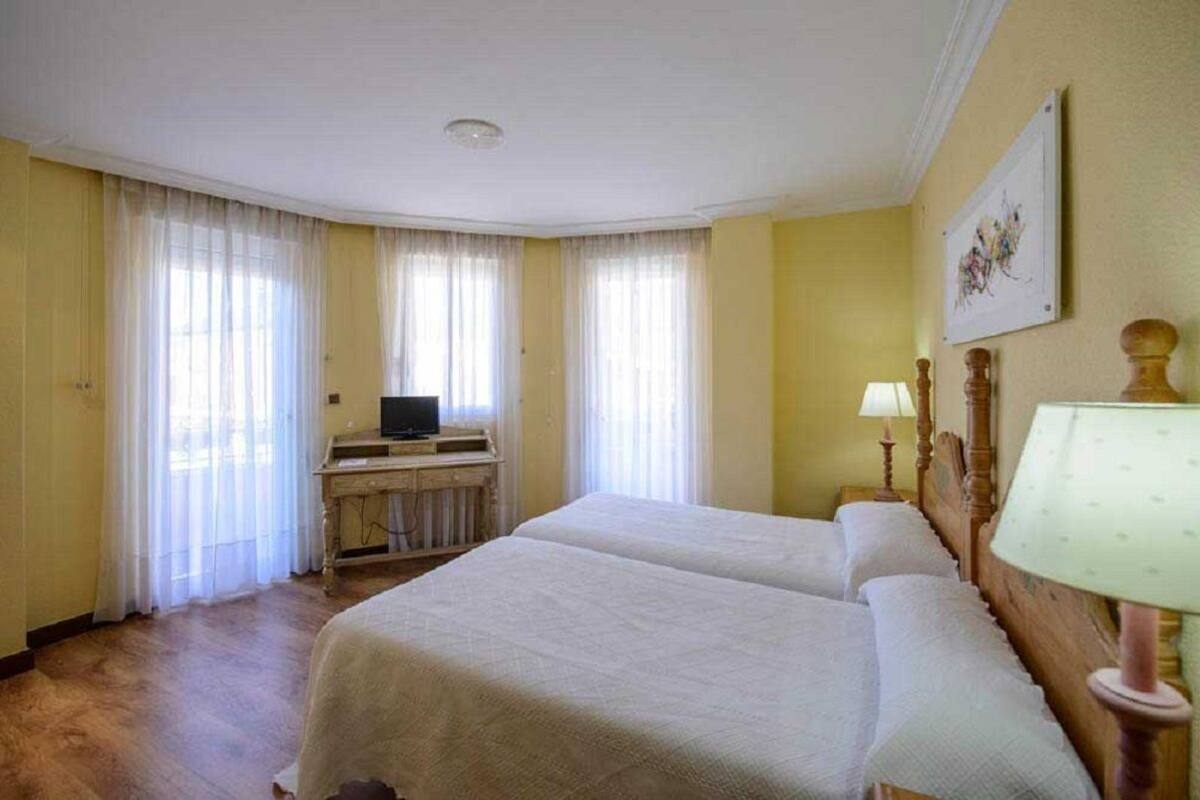 A hotel room with two beds, a desk with a television, and a painting on the wall.
