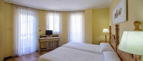 Habitación de hotel con dos camas, un escritorio con televisor y un cuadro en la pared.