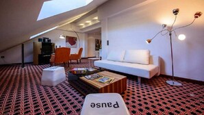 A modern loft apartment with a high ceiling, a skylight, a white sofa, a coffee table, and a patterned carpet.