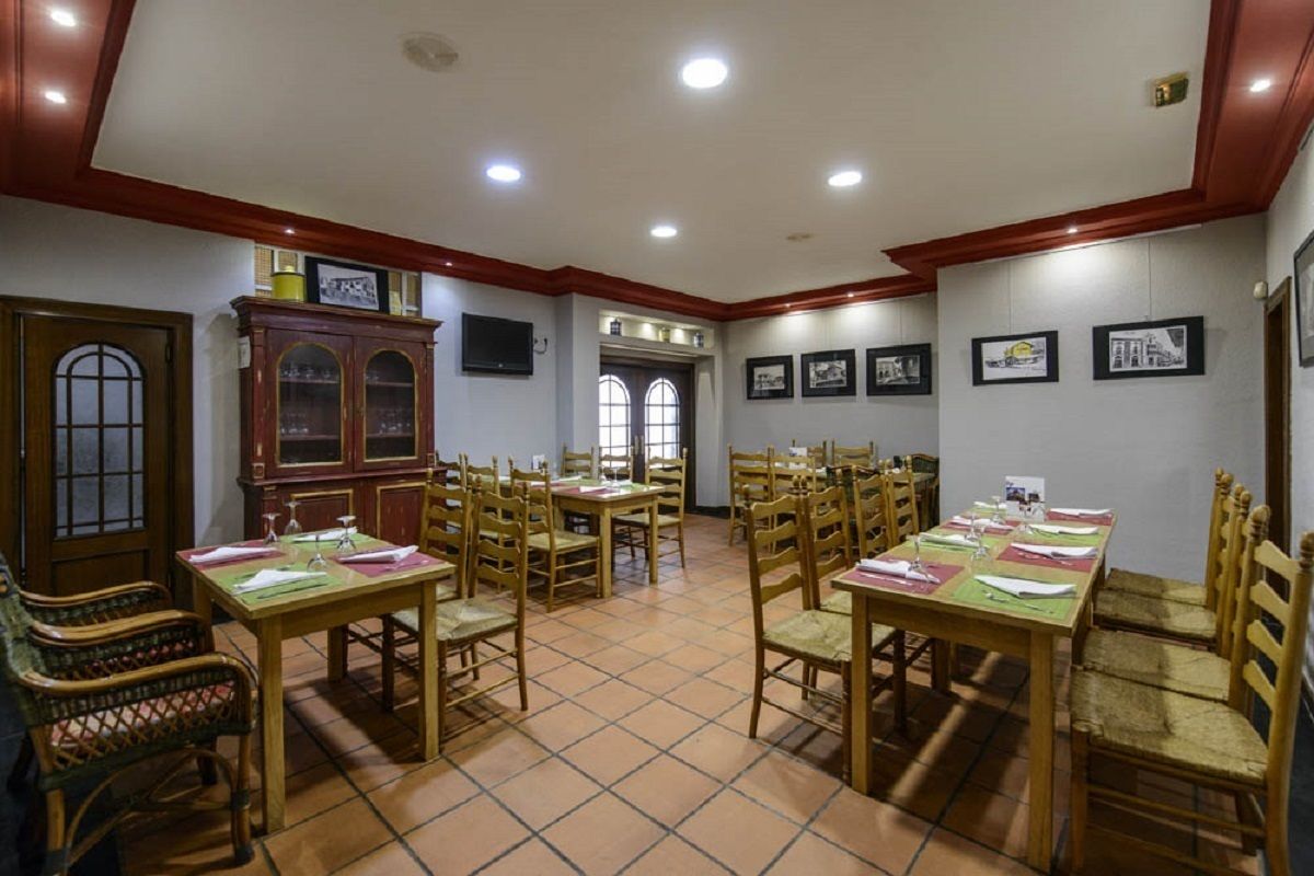 Un comedor con varias mesas y sillas de madera, un mueble de madera grande y cuadros en las paredes.