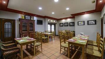 Un comedor con varias mesas y sillas de madera, un mueble de madera grande y cuadros en las paredes.