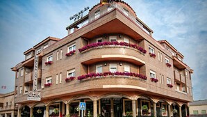 A multi-story hotel with a restaurant on the ground floor, featuring balconies with flower boxes and a prominent entrance with outdoor seating.