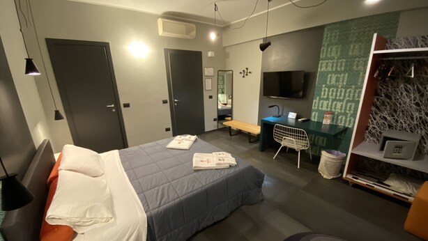 A modern hotel room with a bed, desk, chair, and a TV. - Tiburtina Suites (Rome)