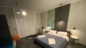 A modern hotel room with a large bed, a bedside table, a nightstand, a wardrobe, and a small round table. - Tiburtina Suites (Rome)