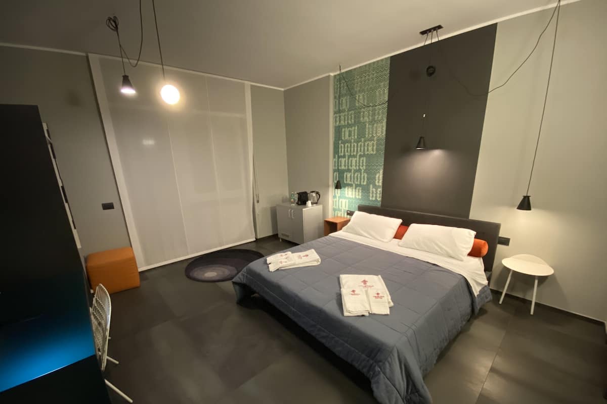 A modern hotel room with a large bed, a bedside table, a nightstand, a wardrobe, and a small round table.