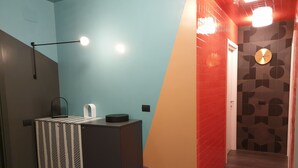 A modern bathroom with a blue and orange wall, a black cabinet, a blue trash bin, and a wall clock. - Tiburtina Suites (Rome)