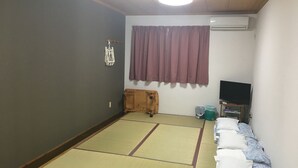 Una habitación con esteras de tatami, una cama futón, un televisor y aire acondicionado.