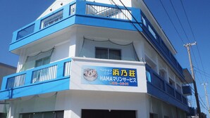 Un edificio de dos pisos con fachada azul y blanca, que presenta un letrero con texto en japonés y un número de teléfono.