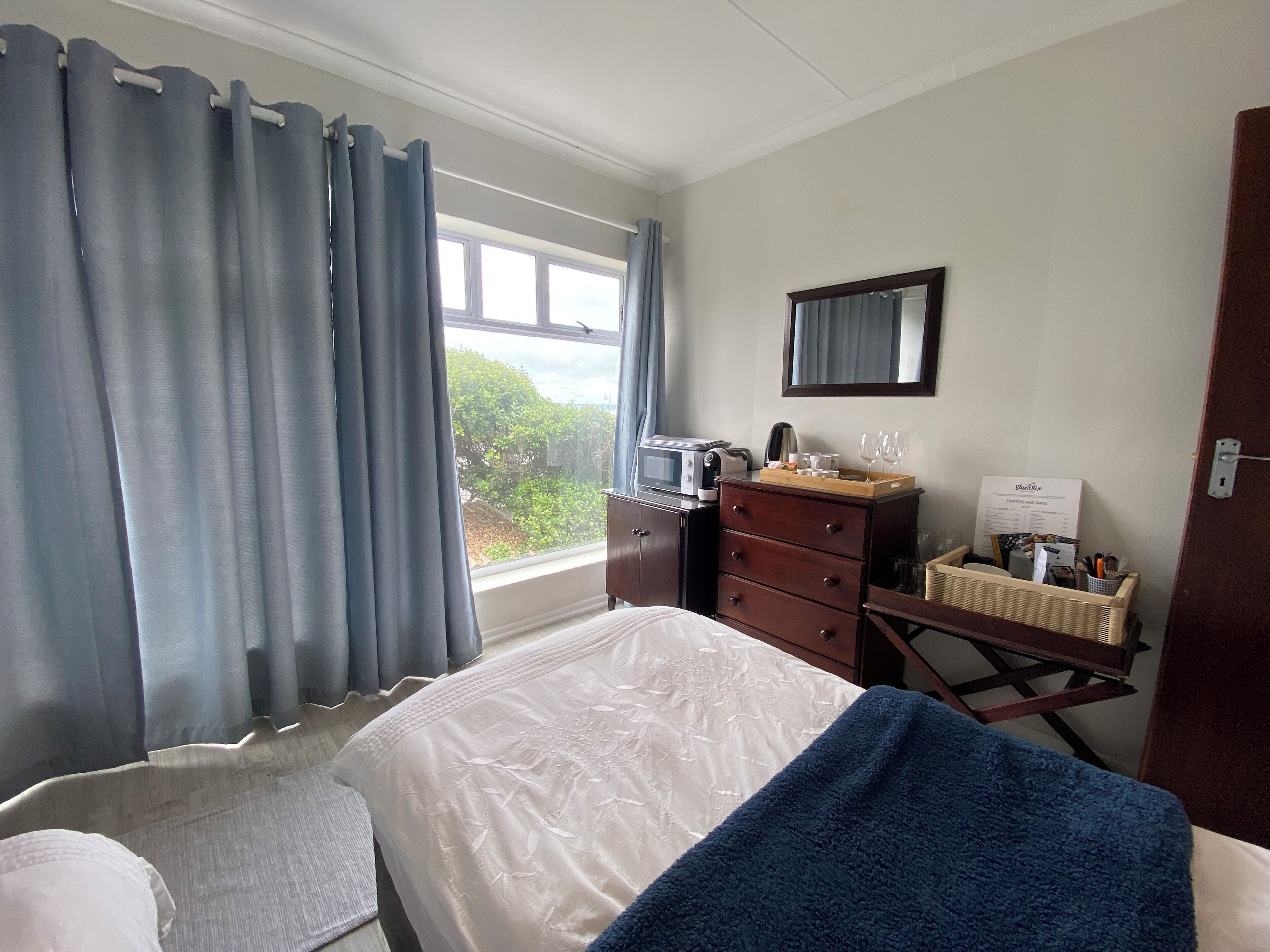 A hotel room with a bed, a dresser, a desk with a computer, and a window with curtains.
