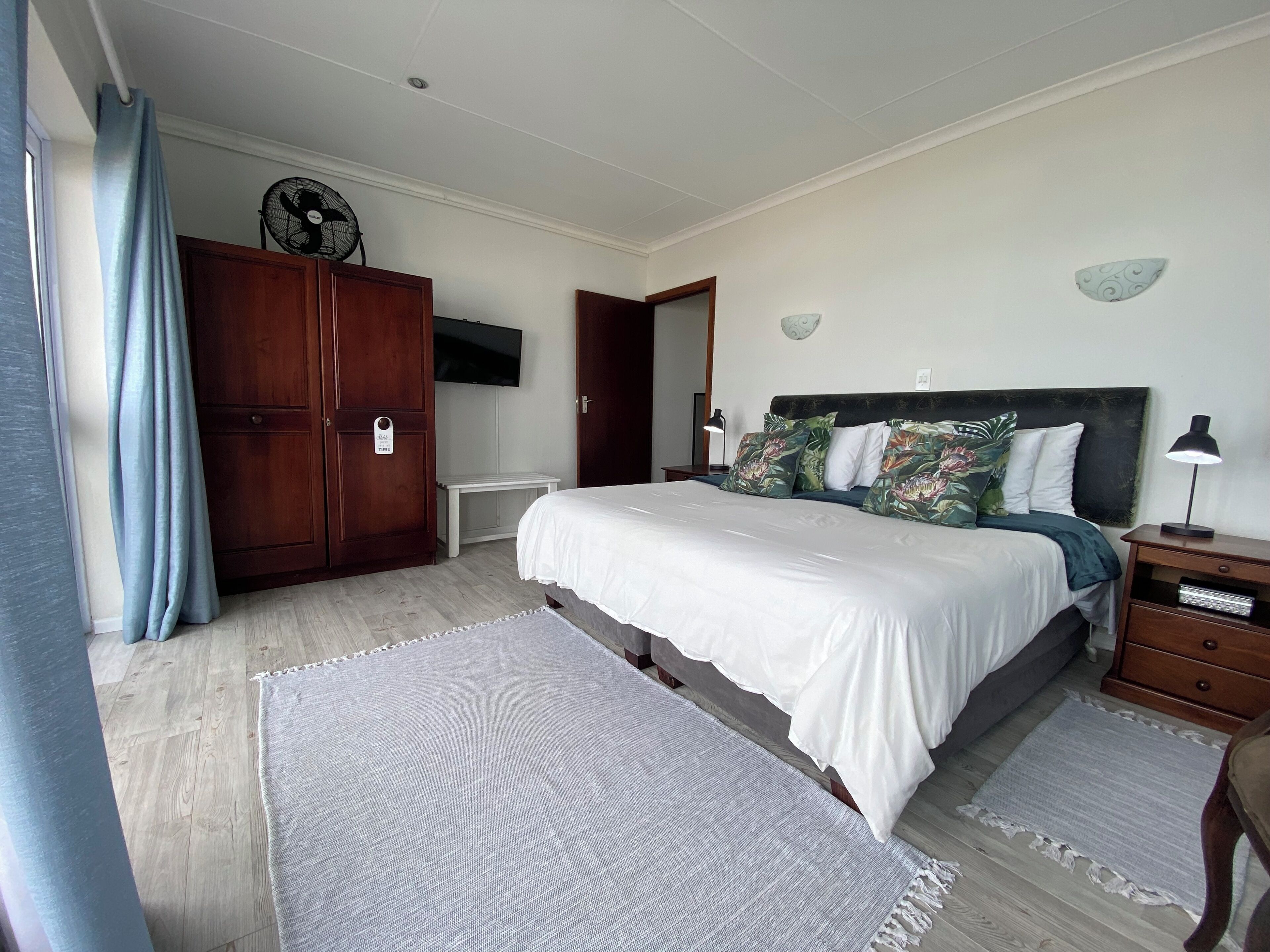 Un dormitorio con cama, un armario de madera, televisor montado en la pared y una mesita de noche con lámpara.