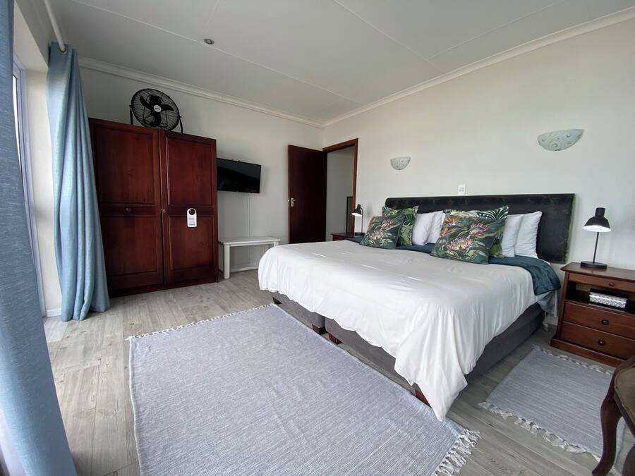 Un dormitorio con cama, un armario de madera, televisor montado en la pared y una mesita de noche con lámpara.