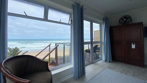 A room with a large window overlooking a beach, a wooden cabinet, and a chair. - Sea Paradise (Wilderness)