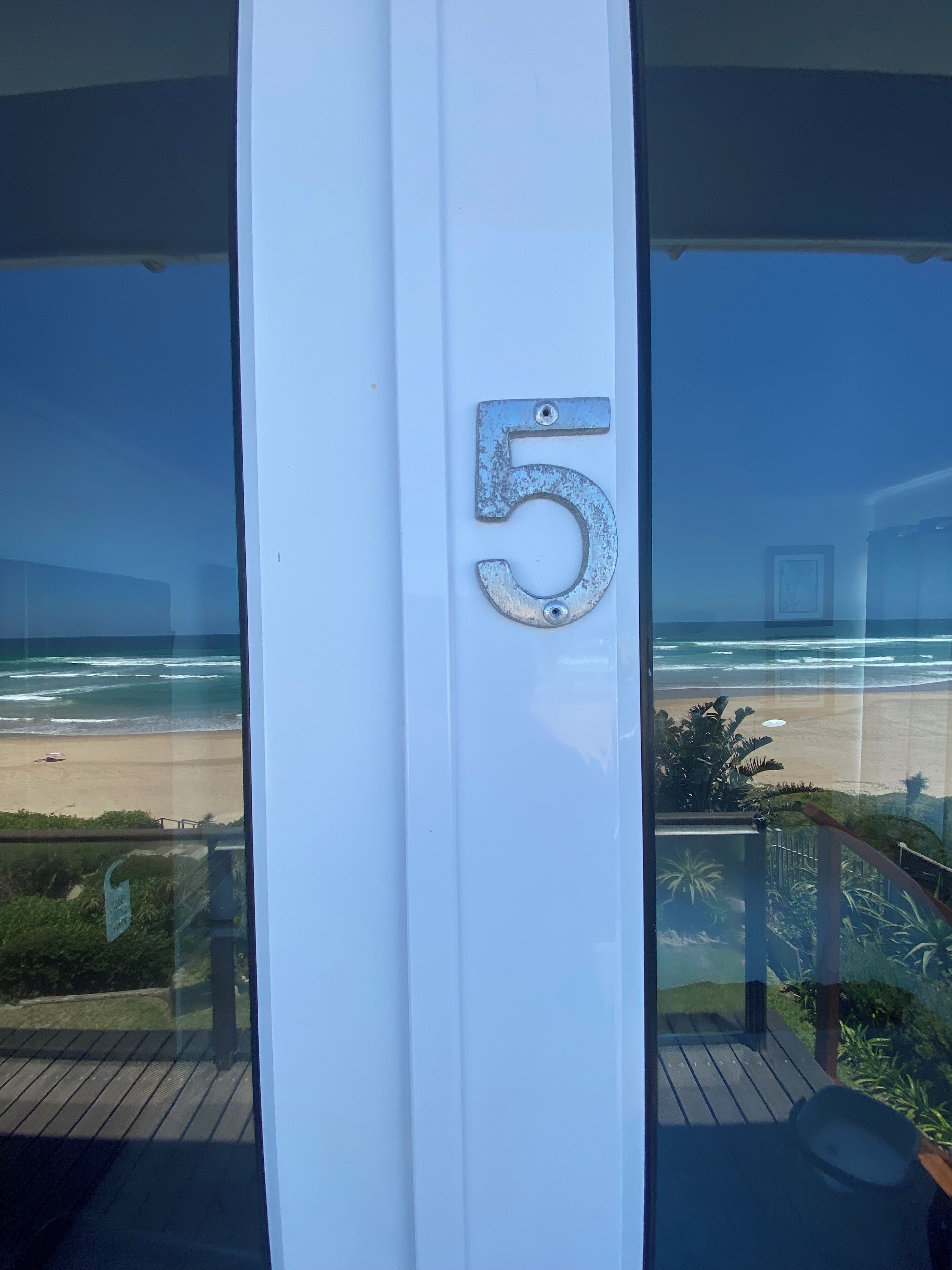 Un número '5' en una puerta blanca, con vista a una playa y al océano a través de amplias ventanas.