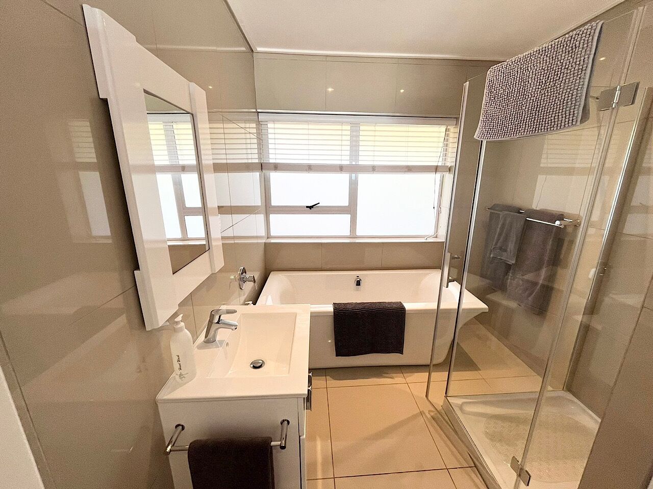 A modern bathroom with a glass-enclosed shower, a large bathtub, and a vanity with a mirror.