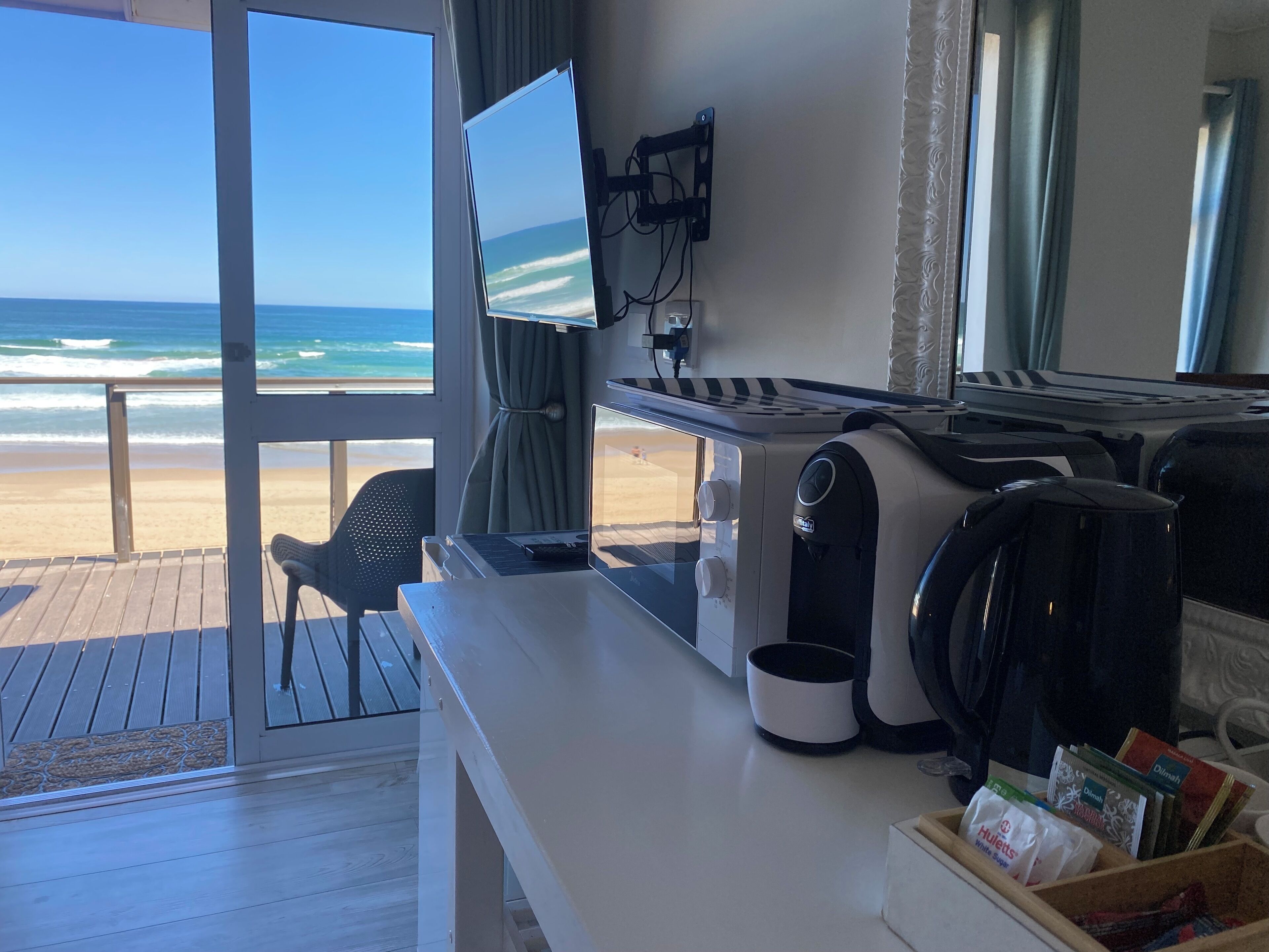 A room with a view of the beach, a desk with a computer, a coffee maker, and a toaster.