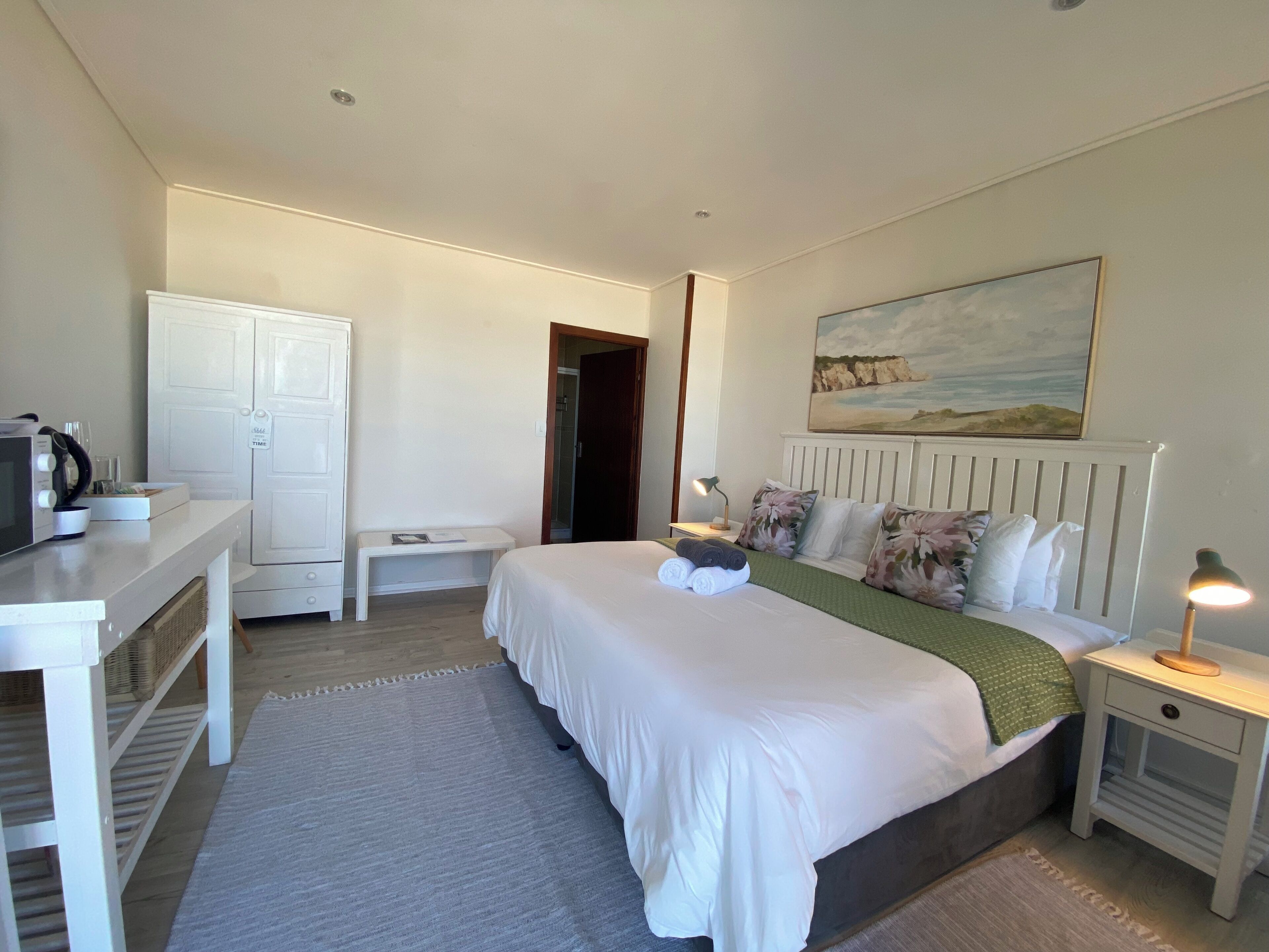 A bedroom with a bed, bedside tables, a desk, a wardrobe, and a painting on the wall.