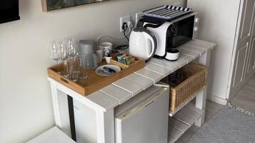 Un angolo cottura con forno a microonde, tostapane e macchina del caffè su un piano di lavoro bianco. Calici da vino e tazze su un vassoio. Un quadro raffigura una spiaggia.