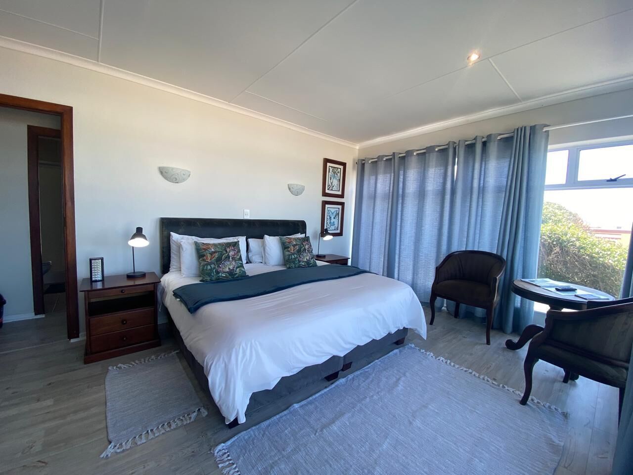 A bedroom with a large bed, a nightstand, a chair, a small table, and a window with curtains.