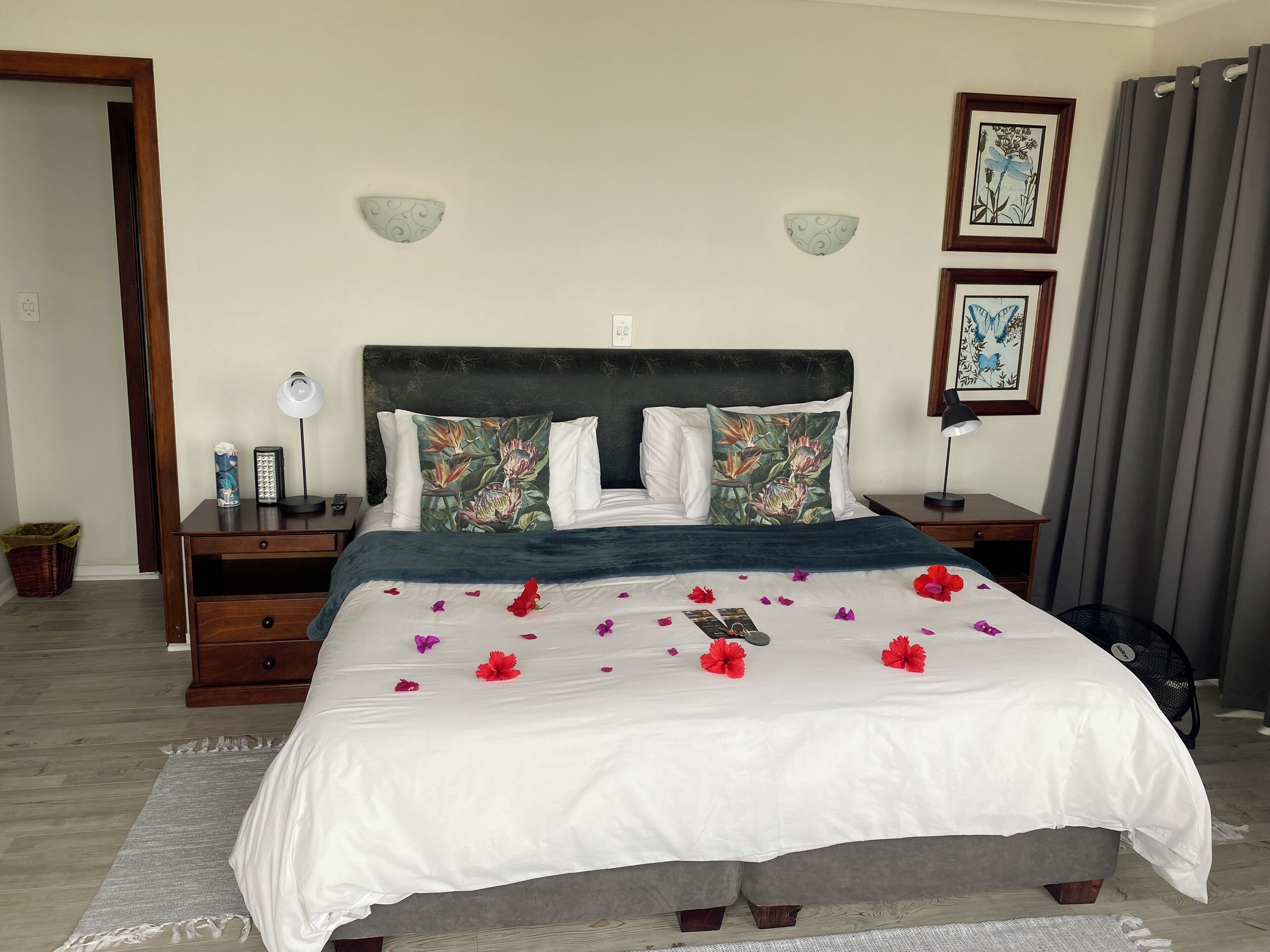 A neatly made bed with white bedding and decorative pillows, a bedside table with a lamp, and a wall-mounted light fixture.