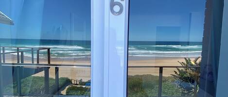 Habitación con vista a la playa, el número '6' en la puerta y una terraza de madera en el exterior.