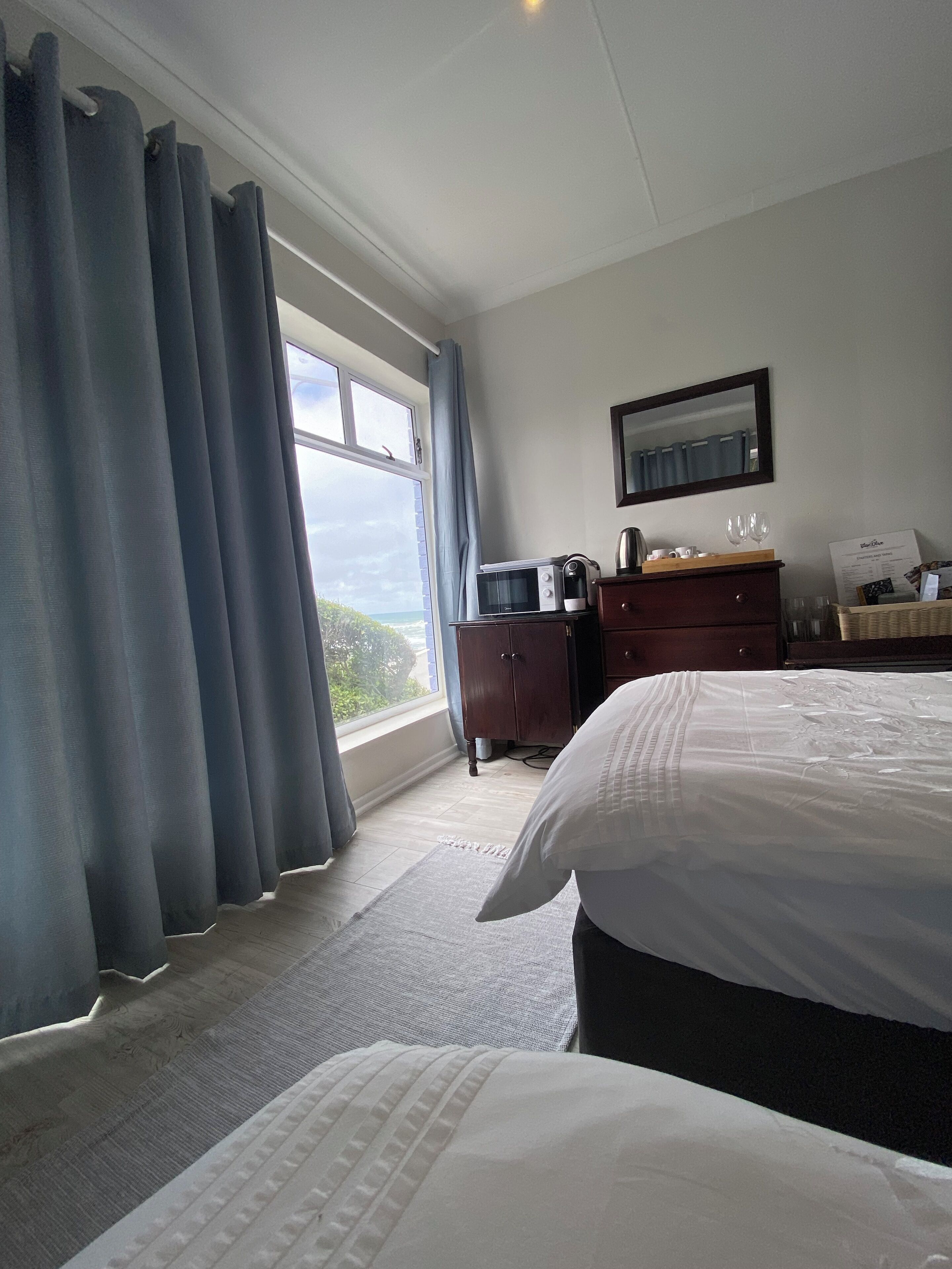 A hotel room with a large bed, a dresser, a microwave, and a view of the outdoors.