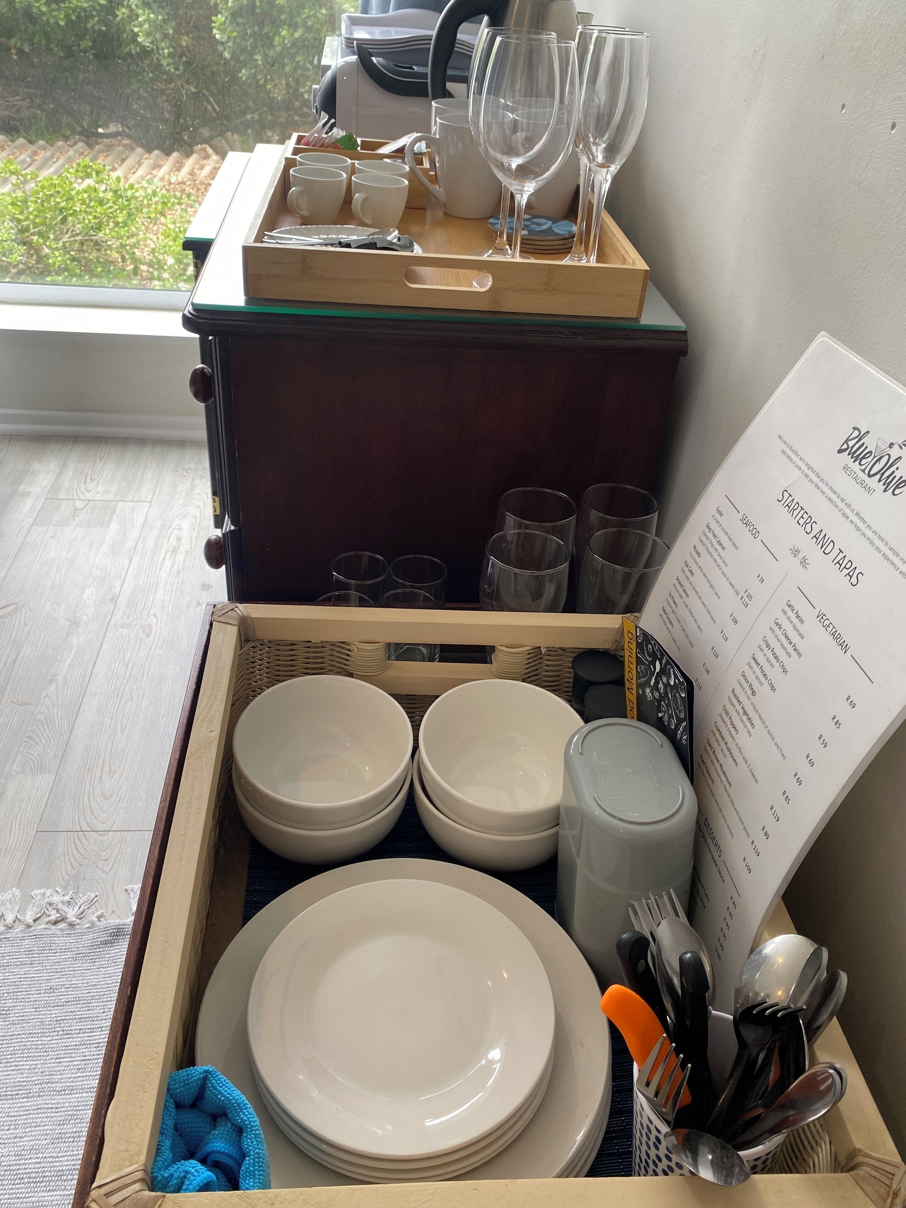 Een rijdend bedieningswagentje met borden, kommen en bestek, en een menu voor Restaurant BlueOlive.