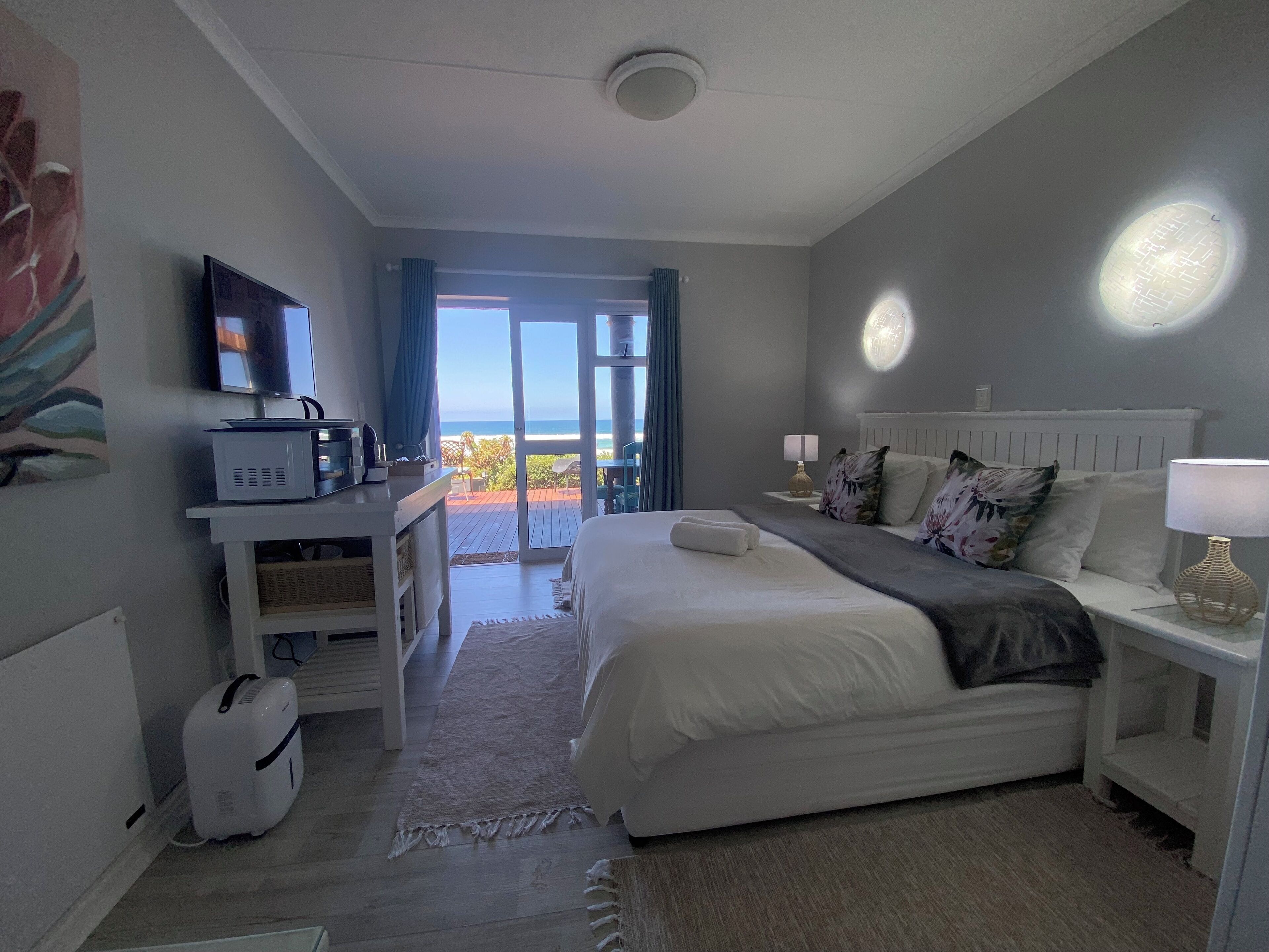 A hotel room with a bed, a desk with a computer, a TV, and a view of the ocean.