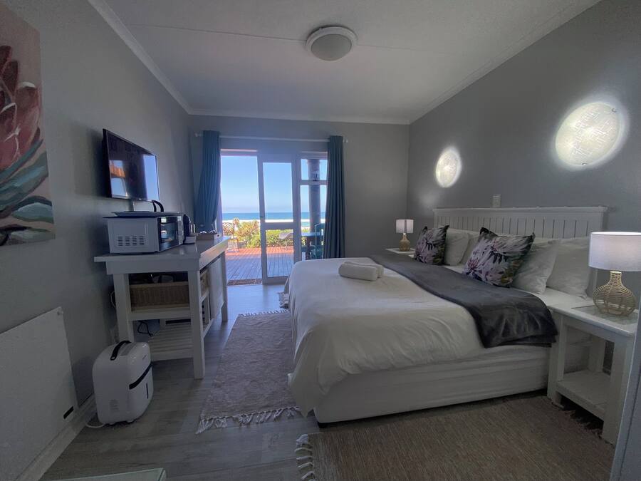A hotel room with a bed, a desk with a computer, a TV, and a view of the ocean.