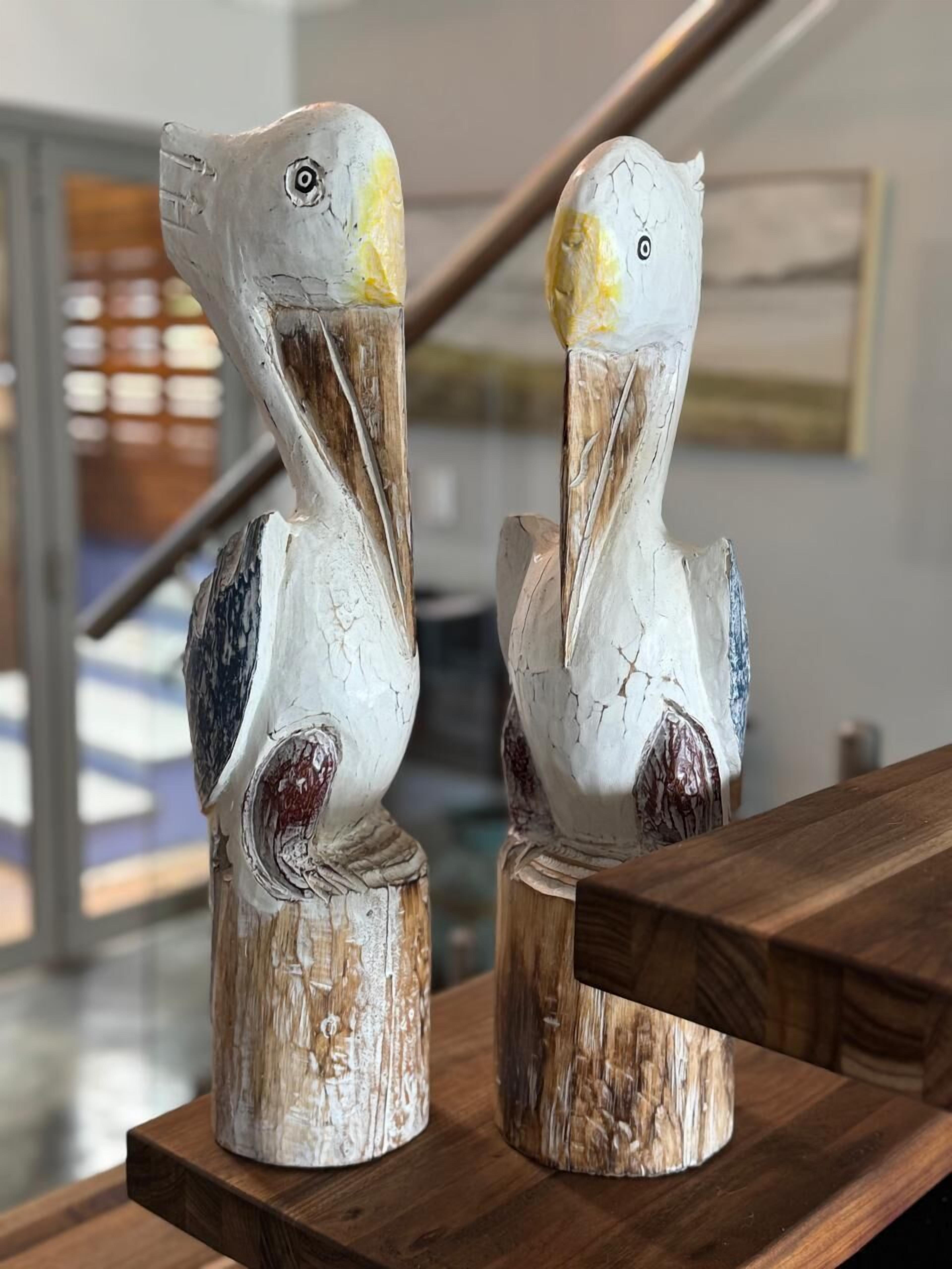 Two wooden sculptures of pelicans on a wooden platform.