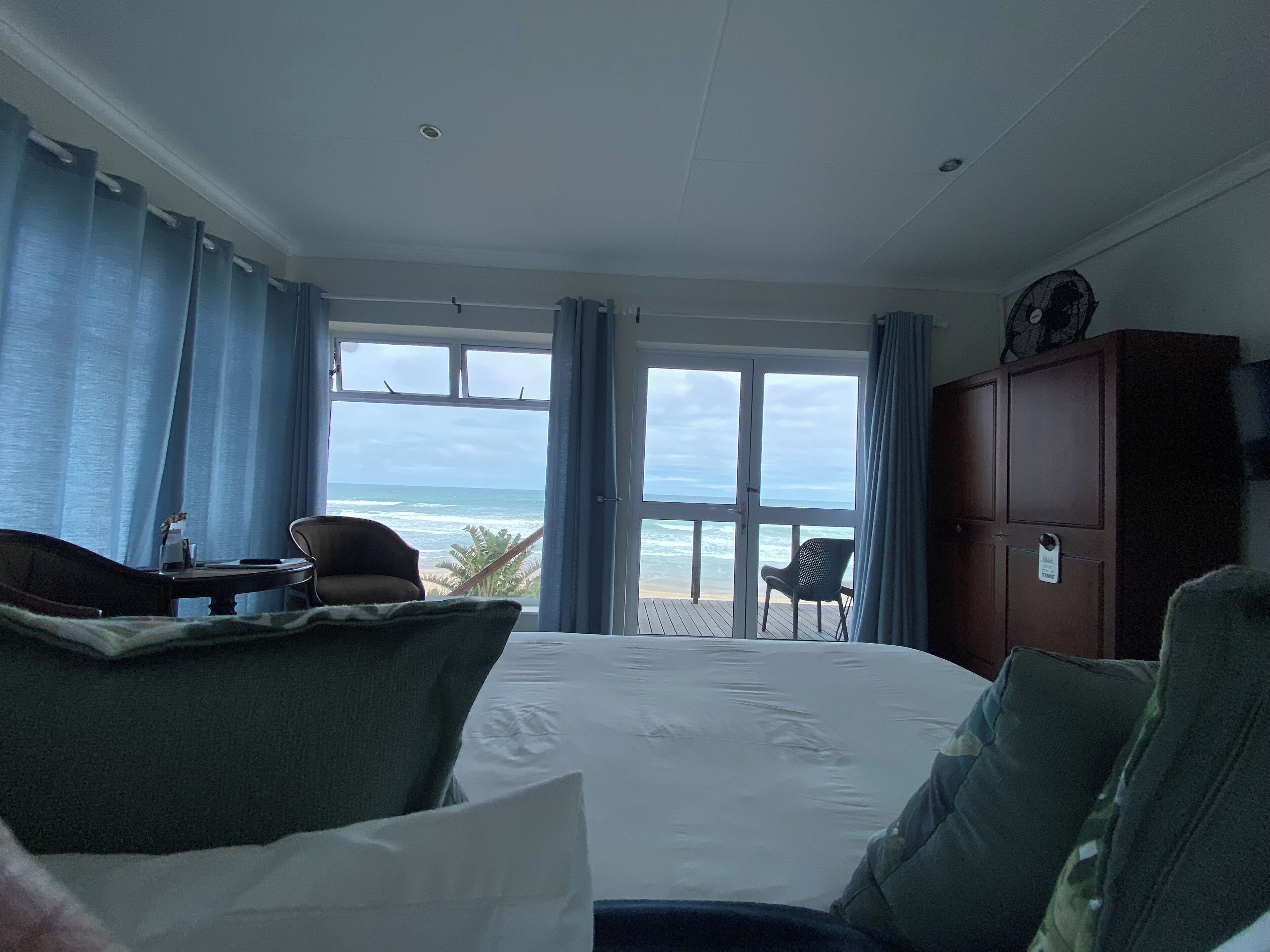 A hotel room with a large bed, a desk, a chair, and a view of the ocean through a sliding glass door.