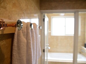 Un baño con un perchero que sostiene tres toallas, una zona de ducha y una puerta que da a otra habitación.