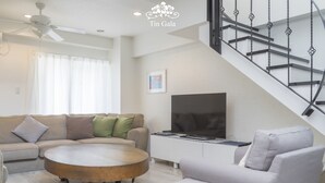 A modern living room with a sofa, a coffee table, a flat-screen TV, and a staircase. - Ocean Villa Tin Gala (Onna)