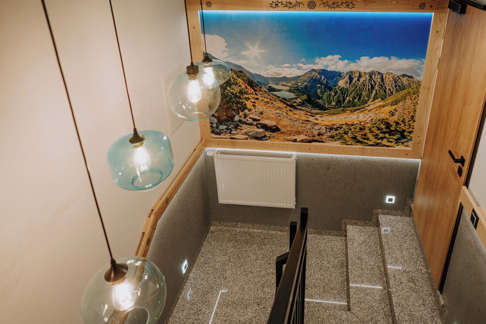 A room with a scenic mural of mountains and a lake, a radiator, and two hanging light fixtures.