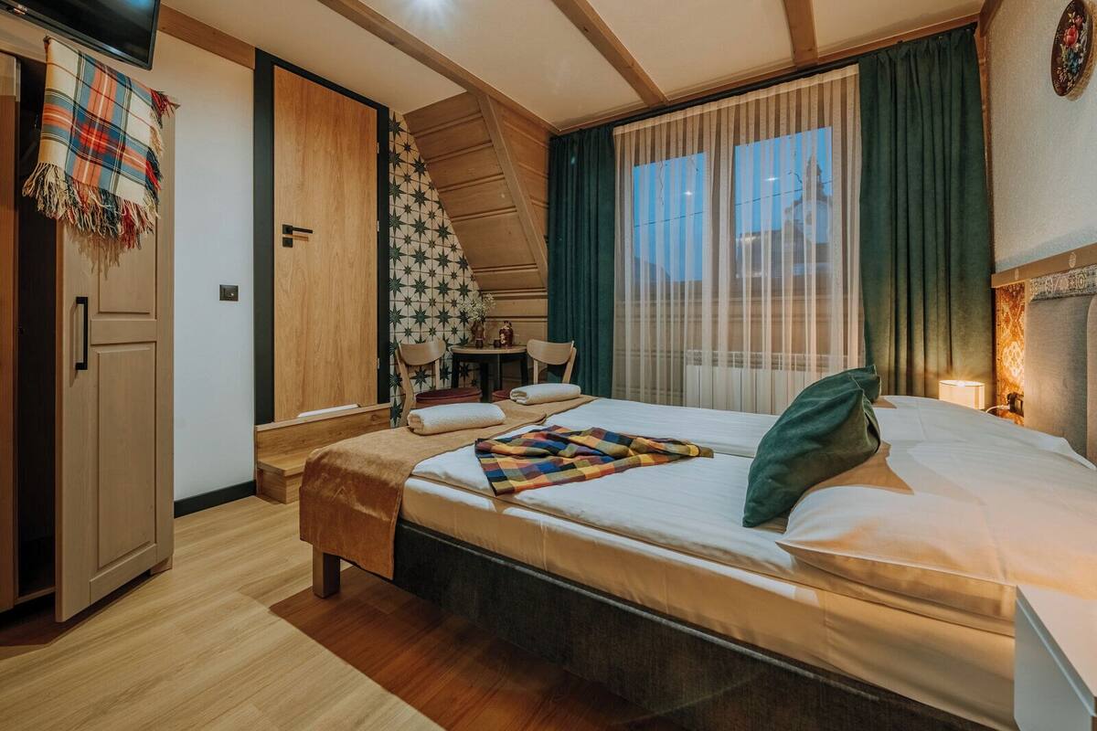 Une chambre à coucher comprenant un lit, une armoire en bois, une petite table avec des chaises, une fenêtre avec des rideaux et un mur orné de carreaux décorés de motifs en étoile.