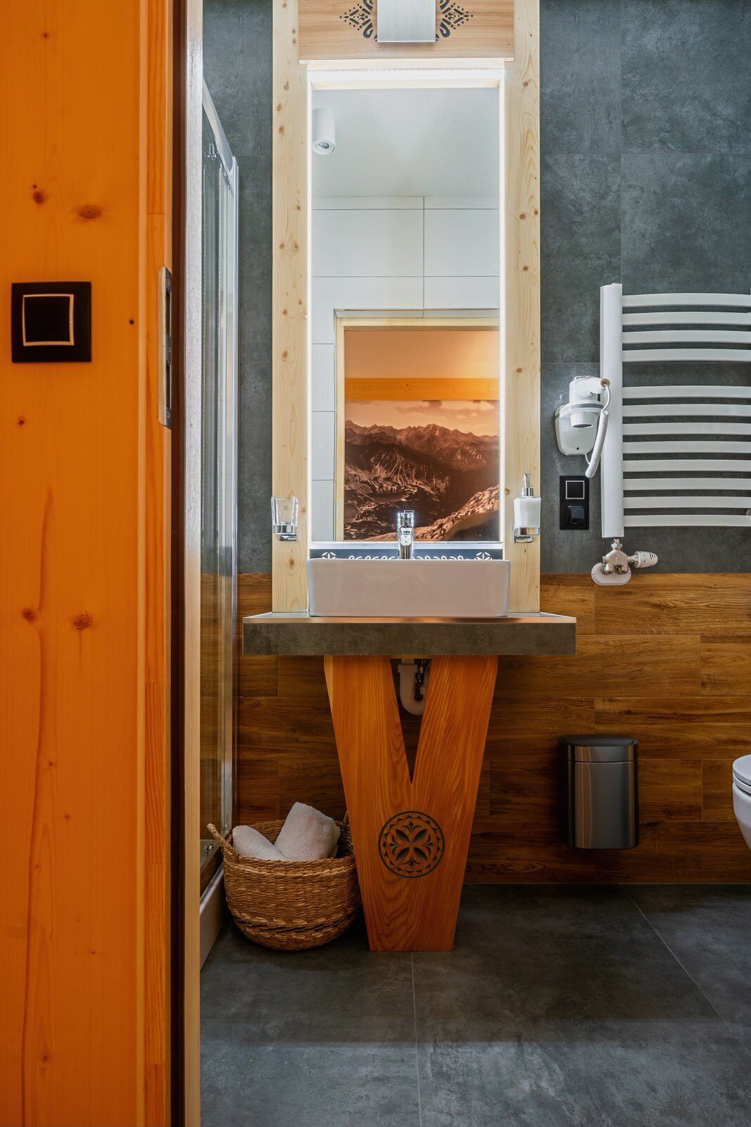 Un baño con tocador de madera, un espejo grande y un cartel con un paisaje de montaña.