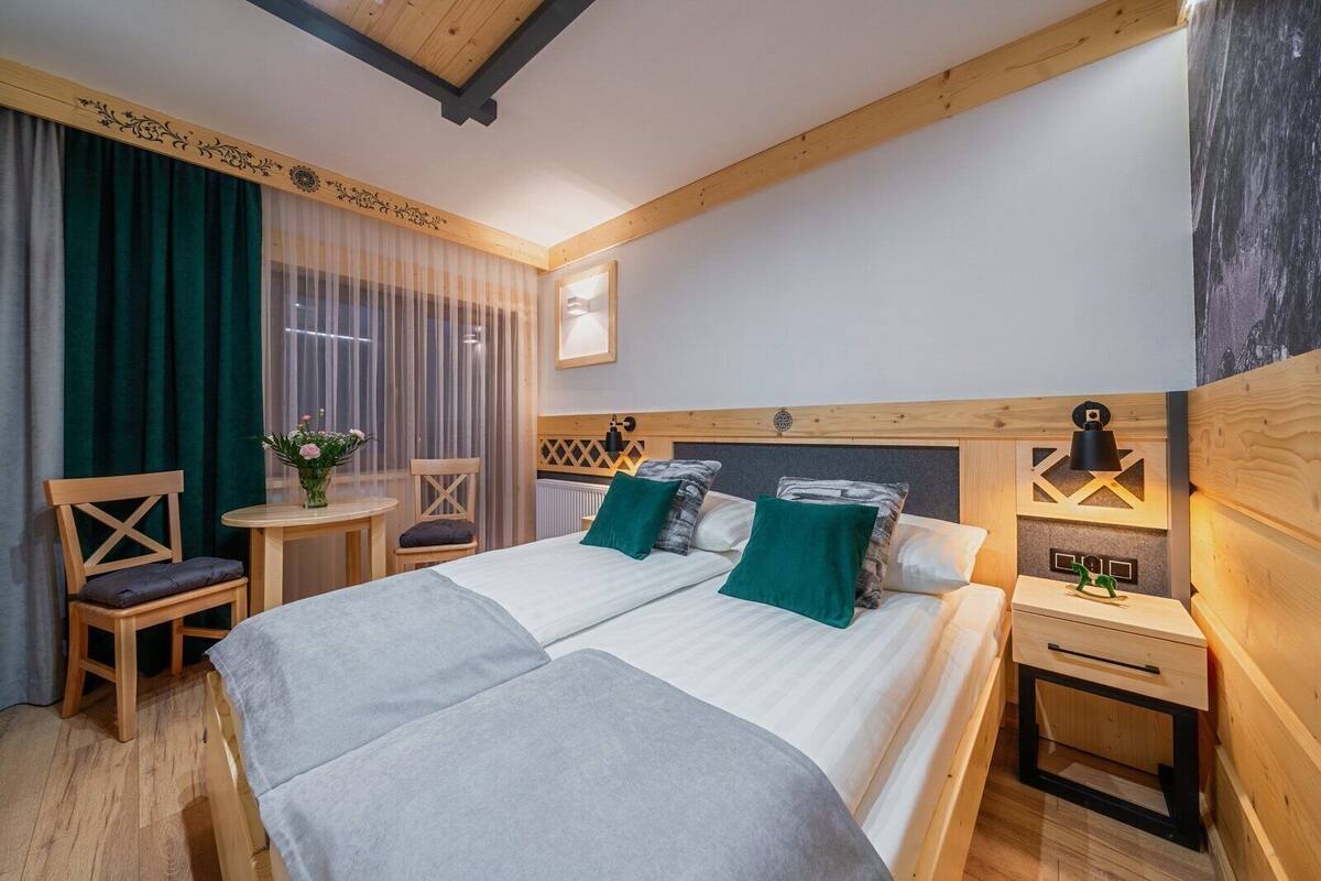 Un lit double avec deux oreillers, une table de chevet avec une lampe, une chaise et une fenêtre avec des rideaux.