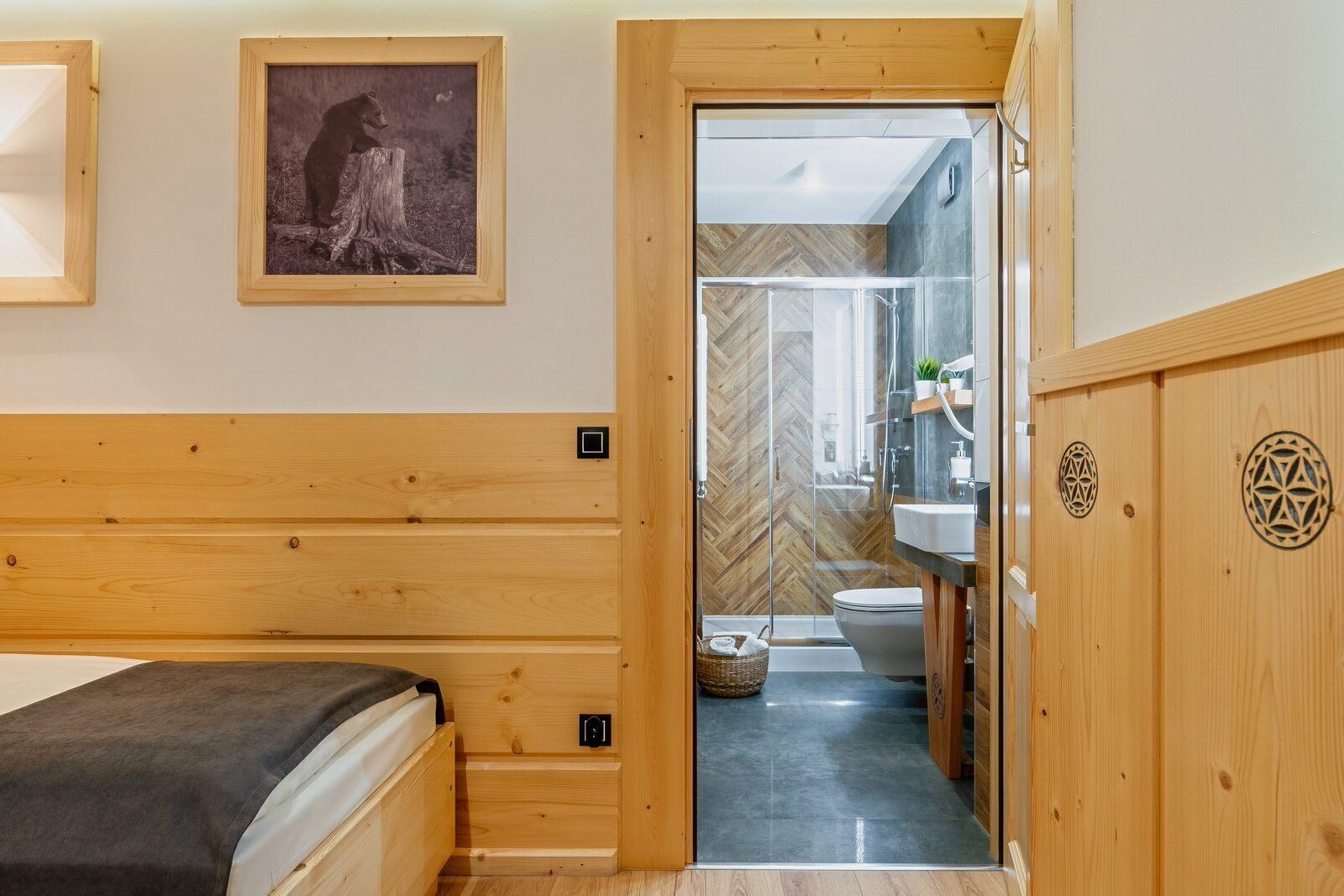 Een kamer met houten lambrisering, een bed, een ingelijste foto en een zichtbare badkamer door een glazen deur.
