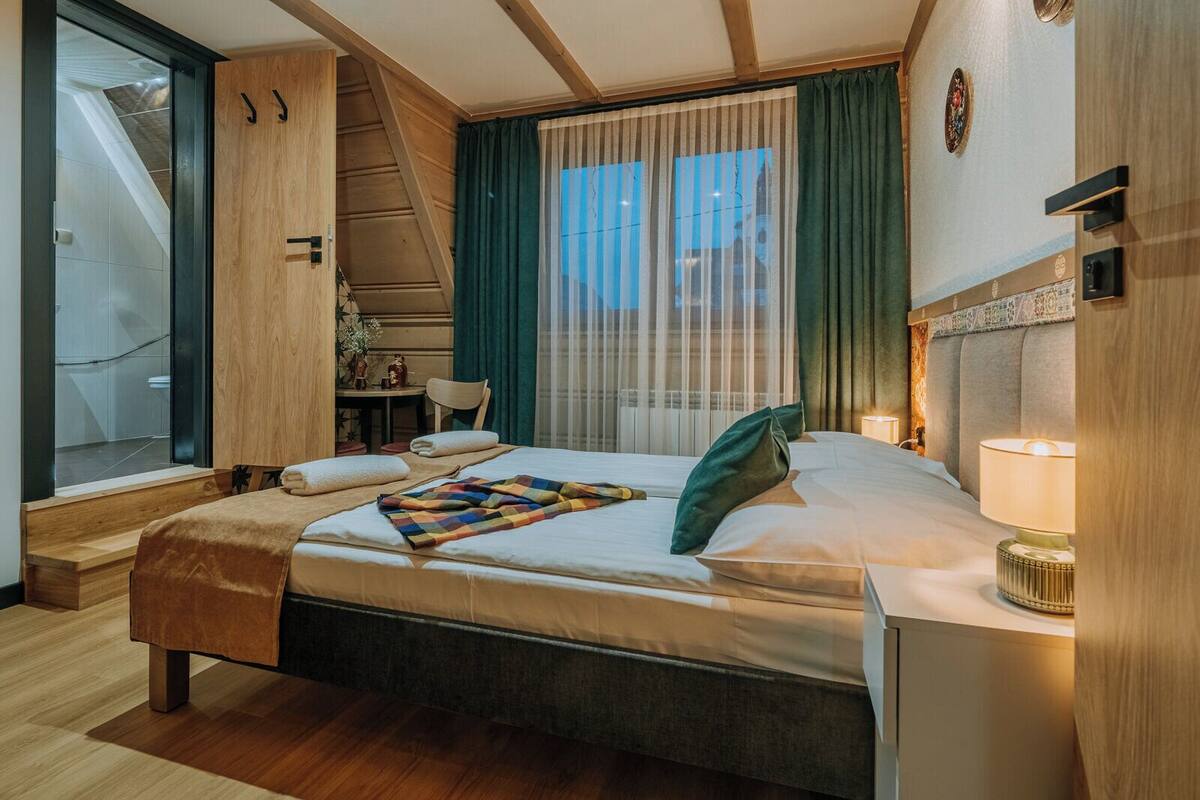 Une chambre d’hôtel moderne dotée d’un grand lit, d’un bureau, d’une chaise, d’une fenêtre avec des rideaux et offrant une vue sur le paysage urbain.
