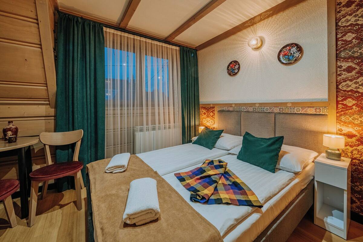 Une chambre d’hôtel avec un lit, deux oreillers, une table avec une chaise et une petite table avec un vase.