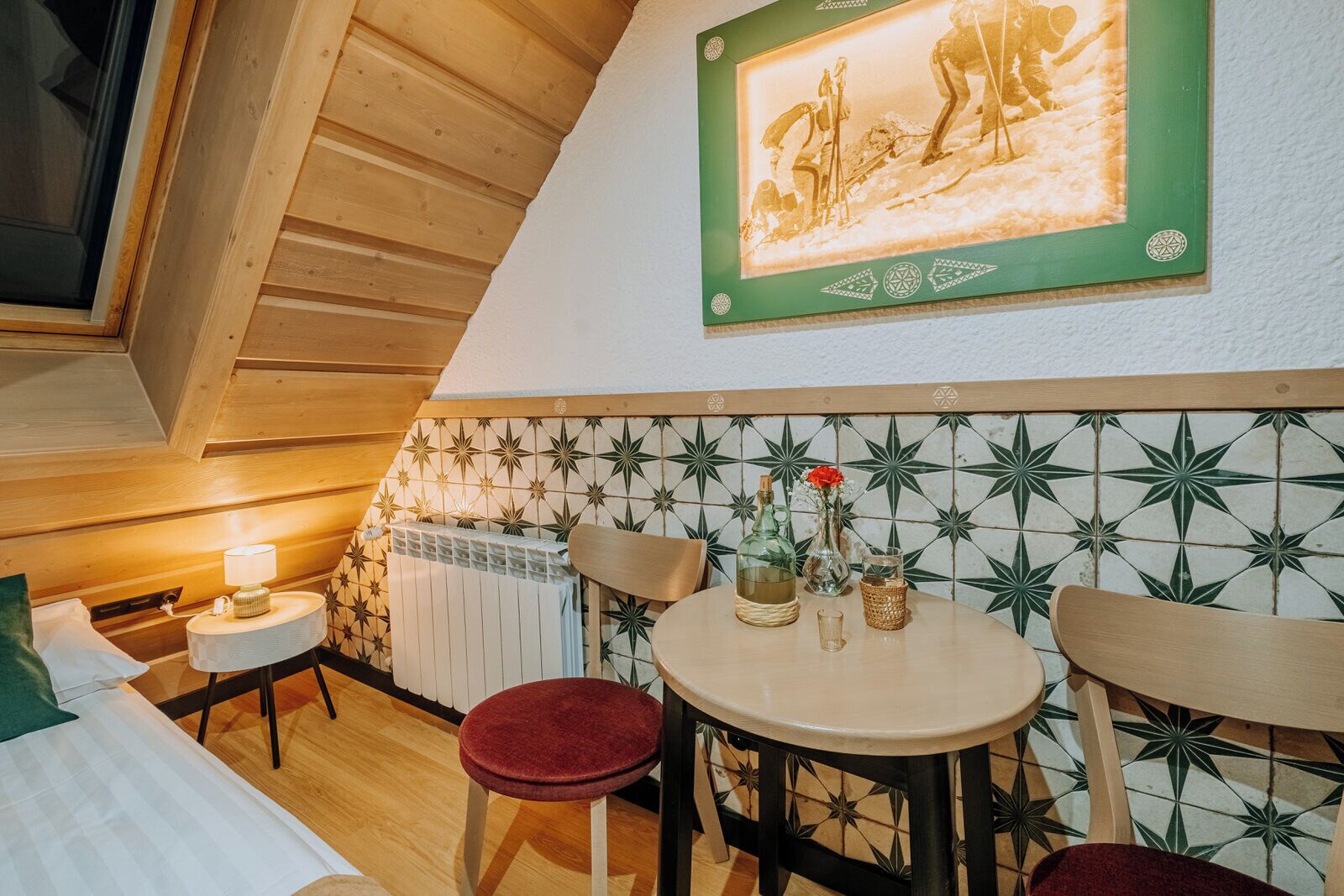 A cozy room with a wooden ceiling, a radiator, a table with chairs, and a framed picture on the wall.