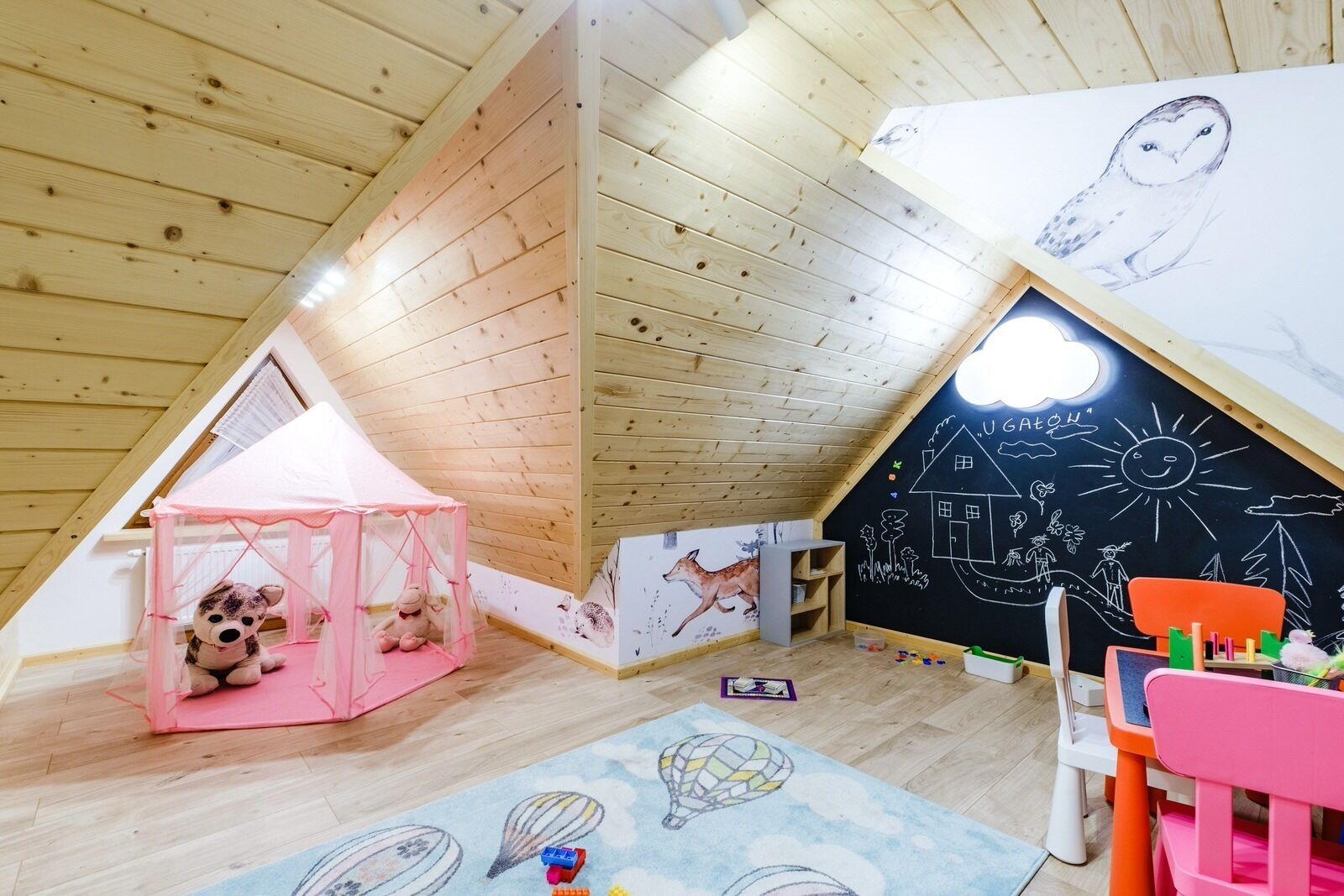 Un cuarto de juegos infantil con una tienda de campaña rosa, una pizarra con dibujos y un techo de madera.