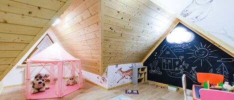 Un cuarto de juegos infantil con una tienda de campaña rosa, una pizarra con dibujos y un techo de madera.