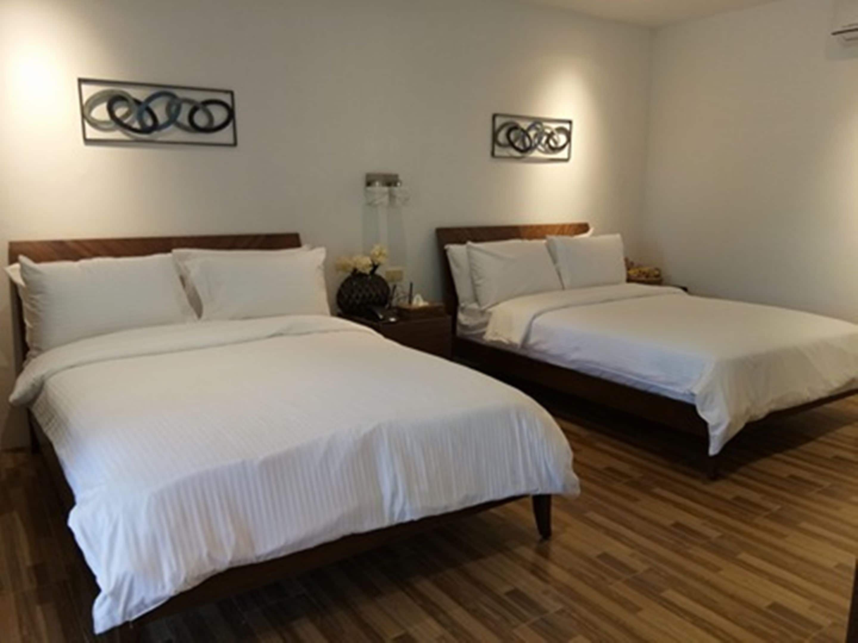 A hotel room with two beds, wooden flooring, and artwork on the walls.