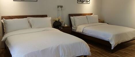 A hotel room with two beds, wooden flooring, and artwork on the walls.