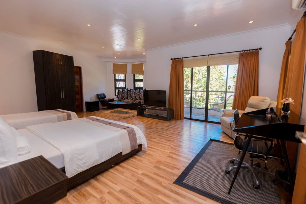 Ein Hotelzimmer mit zwei Betten, einem Schreibtisch, einem Fernseher und einem Balkon mit Vorhängen.