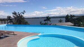 A swimming pool with a wooden deck and lounge chairs, overlooking a body of water and trees. - Bellagio Hills Hotel and Restaurant (Paoay)